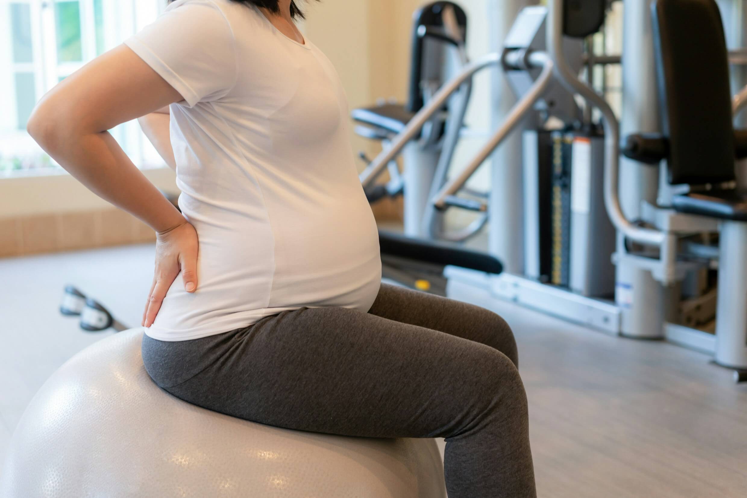 Pregnant woman experiencing lower back pain while sitting on an exercise ball | Castine Concierge Physical Therapy | Mobile Physical Therapy Services Washington DC